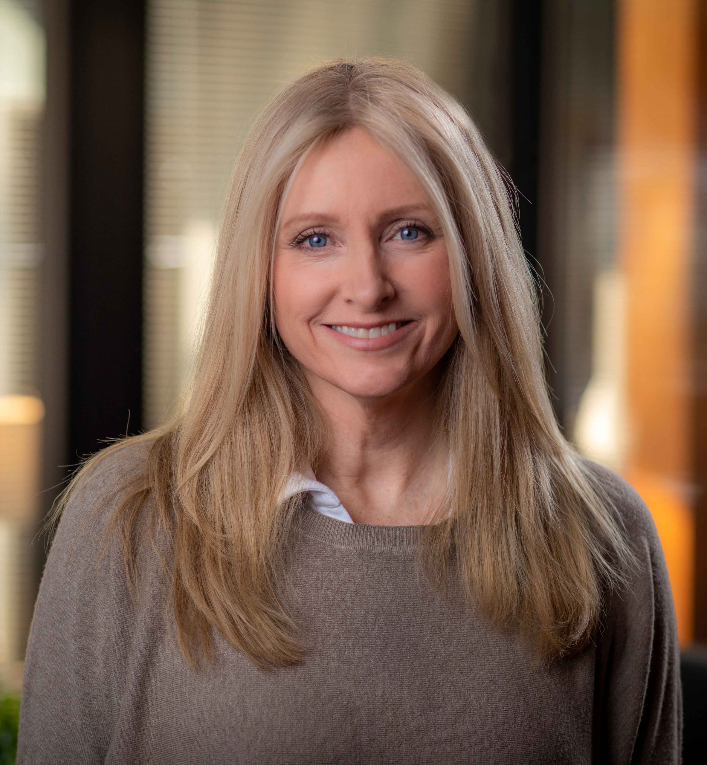 A headshot of a blonde white female in a brown sweater