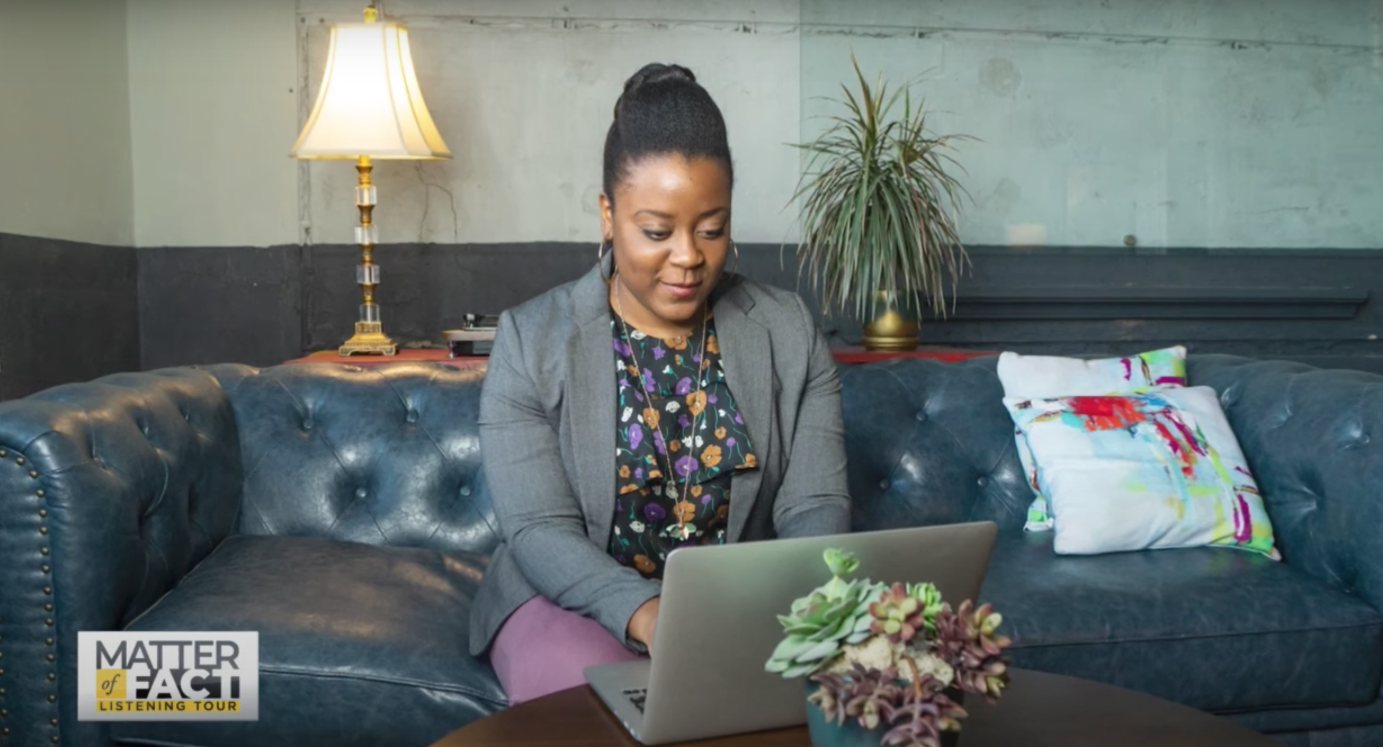 Dr. Nashlie Sephus sits on a ble leather couch and appears to be working on a laptop