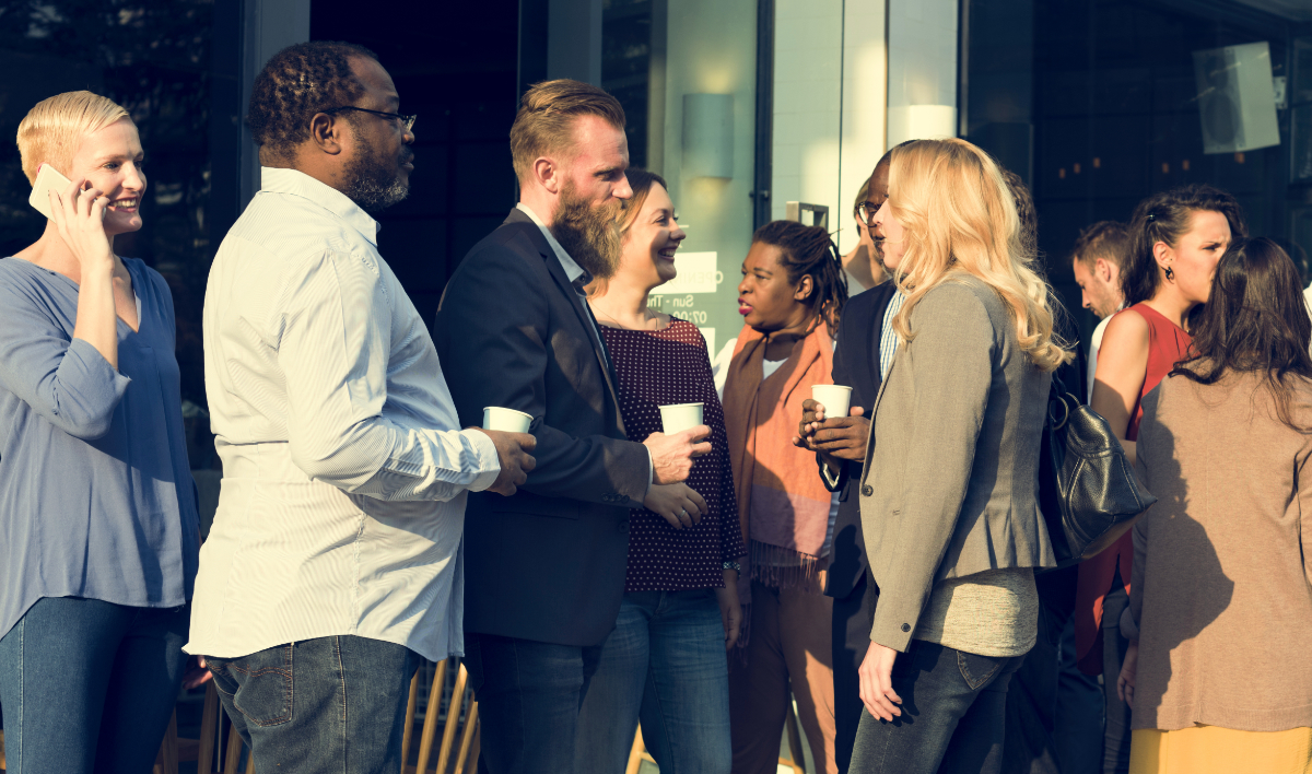 A group of diverse professionals stand outside of a modern looking building talking and networking