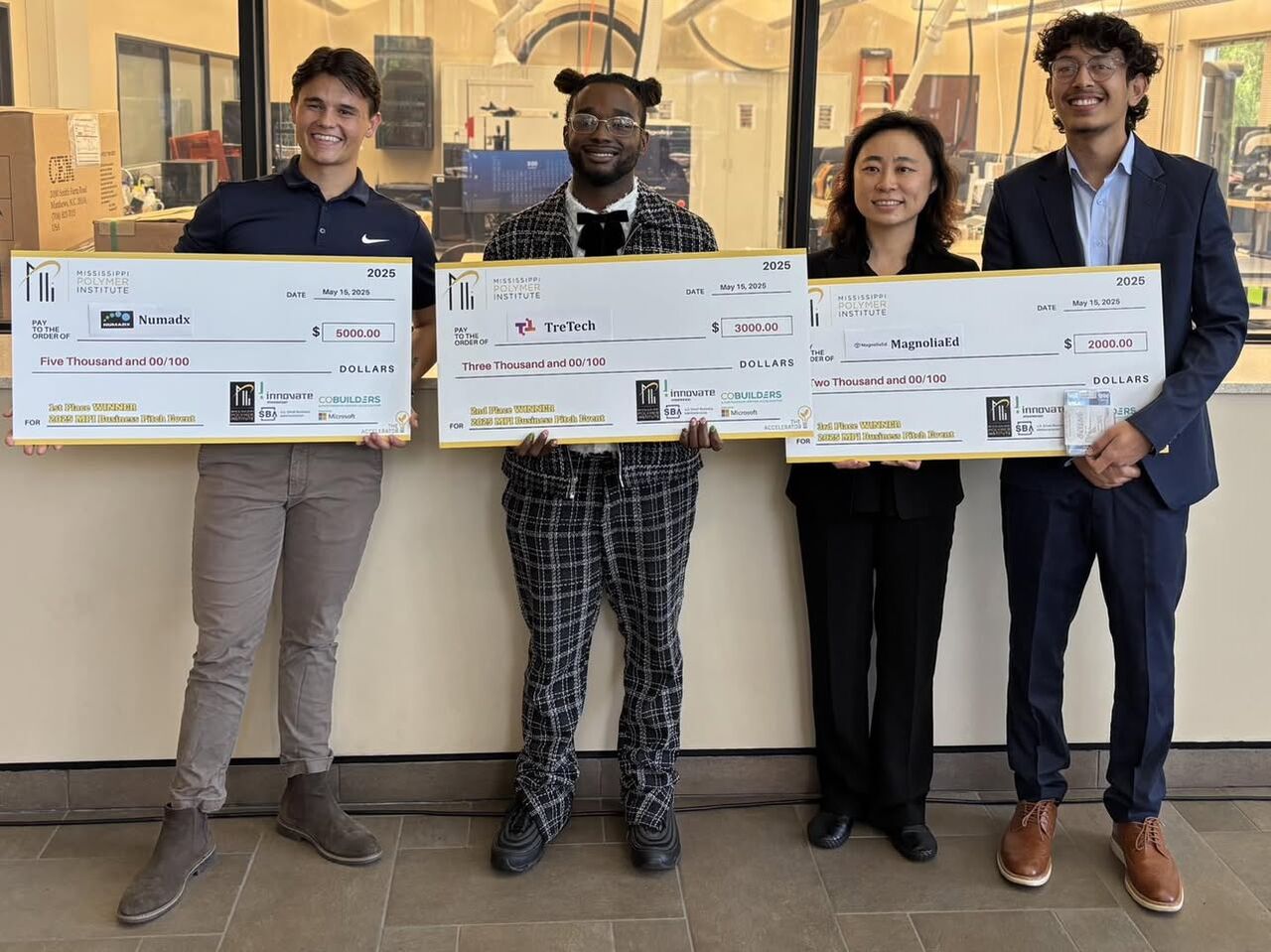 Four founders stand together smiling holding giant checks.